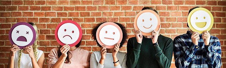 Ein Reihe Menschen, die sich Smiley-Schilder vor das Gesicht halten